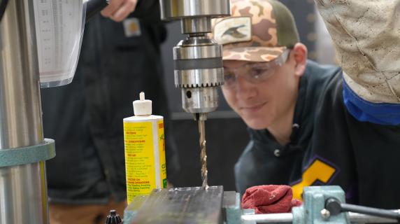 a young man in a camo hat works a drill in the LCC construction trades workshop