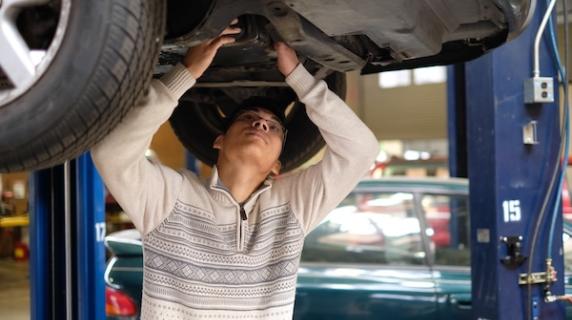 an automotive student repairs on a car from underneath