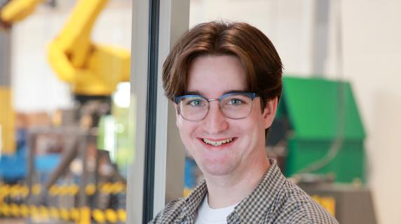 Thatcher, a student standing with their arms crossed looking into the camera wearing a green shirt over a white tee-shirt