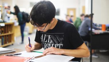 Student studying at a table surrounded by papers and notebooks 