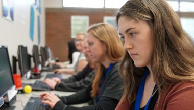 Students lined up at a long table using computers