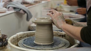close up of a person forming a clay vase on a throwing wheel