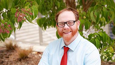 Headshot of Douglas, outside with a bright red tie. 