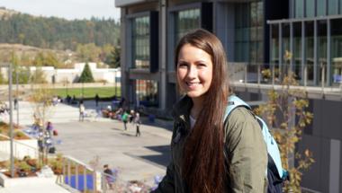 A young woman with a backpack smiling in front of Center Building on main campus