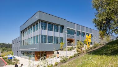 The exterior of the ITEC building on a sunny day with students and the bright yellow statue in front