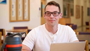 a scholarship winner, a young manwith glasses, working on a laptop