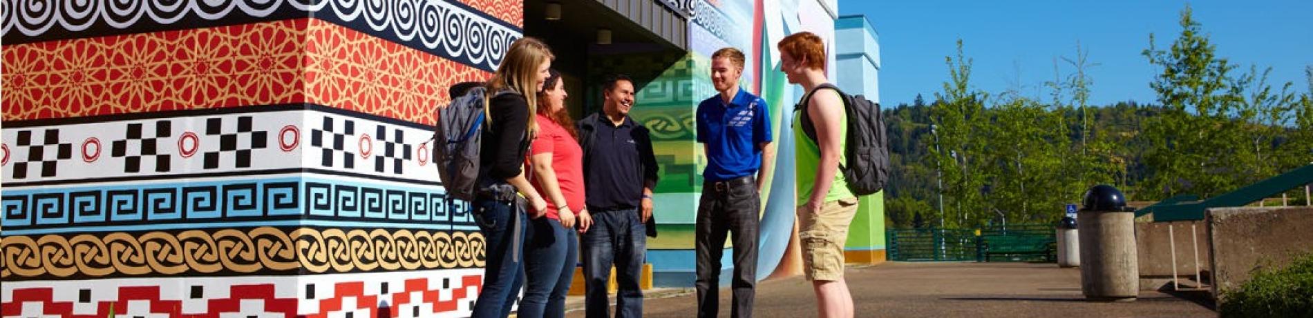 a group of people chatting at the corner of a building with a mural 