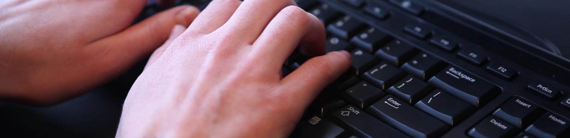close up of hands typing on a black keyboard.