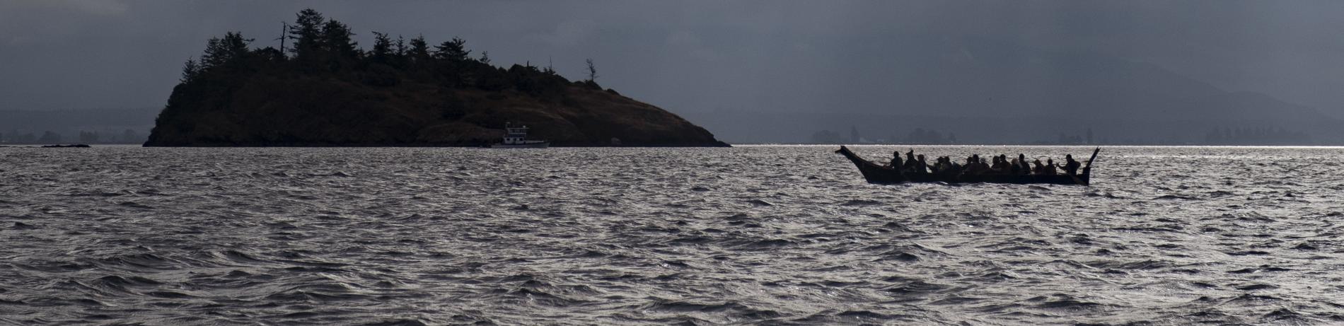 A traditional canoe paddling on a lake with an island in the background