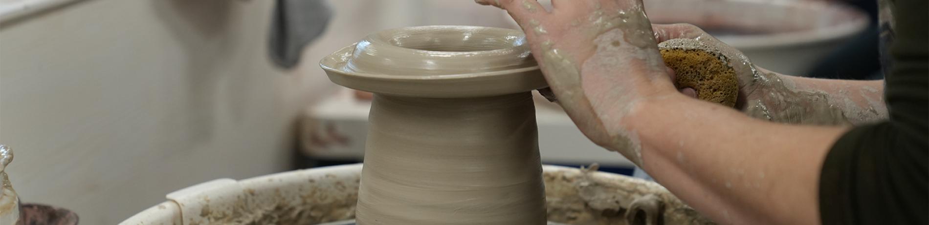 close up of a person forming a clay vase on a throwing wheel