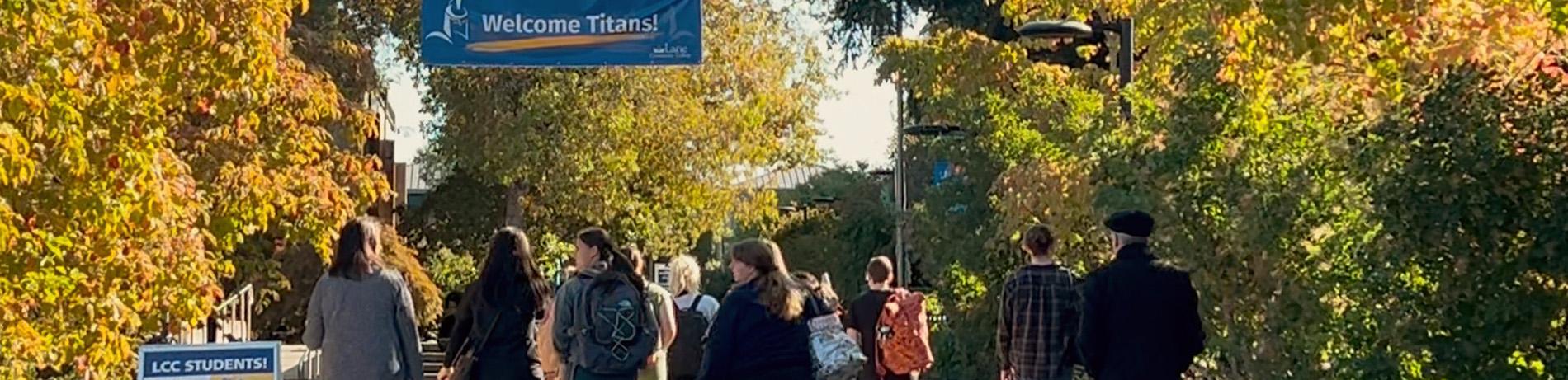 high school students talk to friends and walk to class under a "welcome titans" banner at the entrance of campus on a fall day