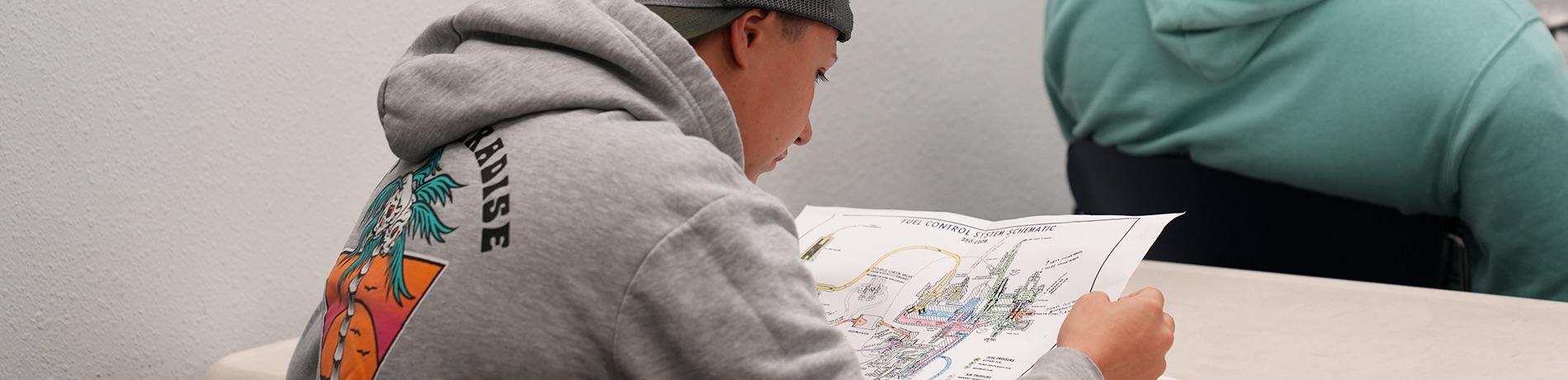 student wearing a hoodie studies a fuel control schematic in a classroom