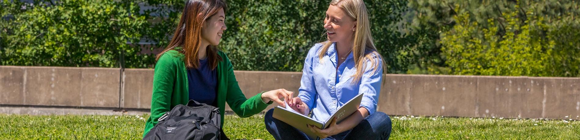 two students sitting on the grass discussing schoolwork