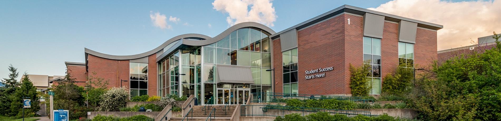 Building 1, a brick building with a swoopy roof, on main campus on a sunny day