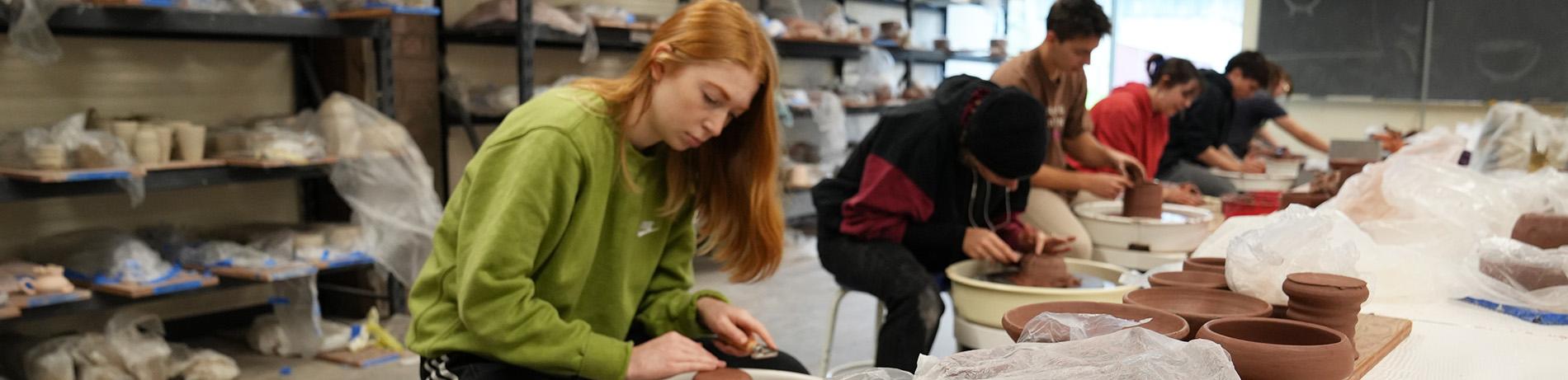 art students throwing clay on wheels in a classroom
