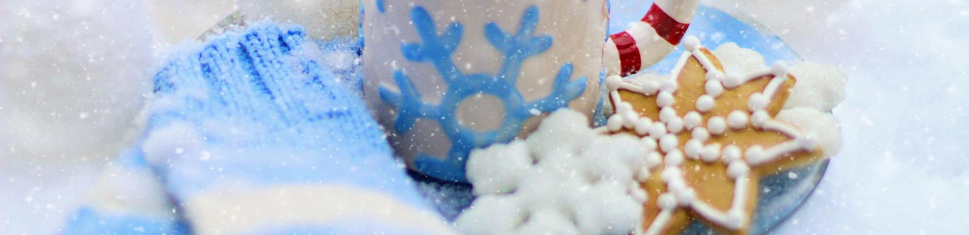 blue gloves, a mug of hot chocolate, and snowflake cookies with sparkling snow in the background