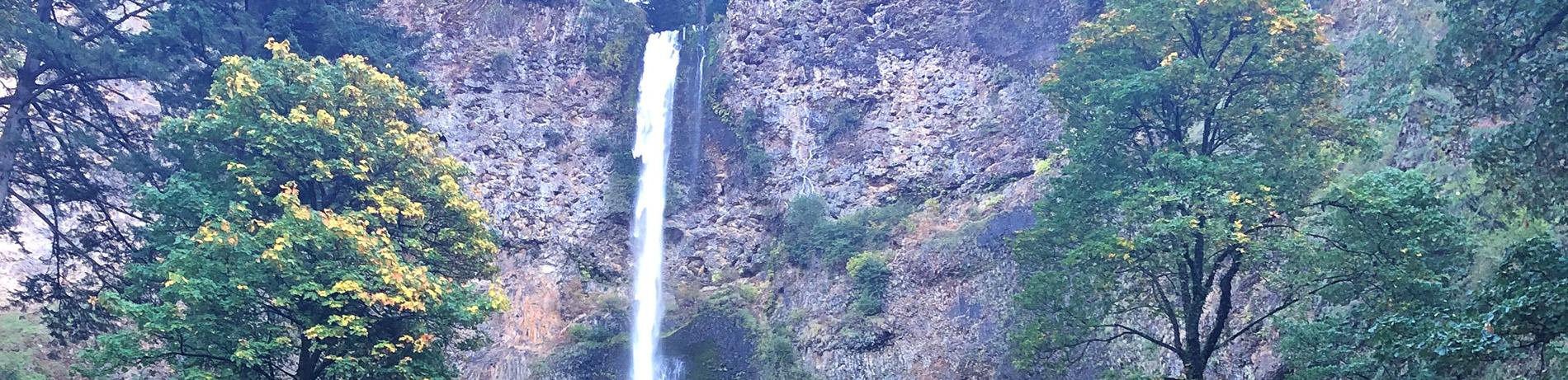 the top of Multnomah Falls spilling over basalt rocks and framed by trees just starting to turn yellow