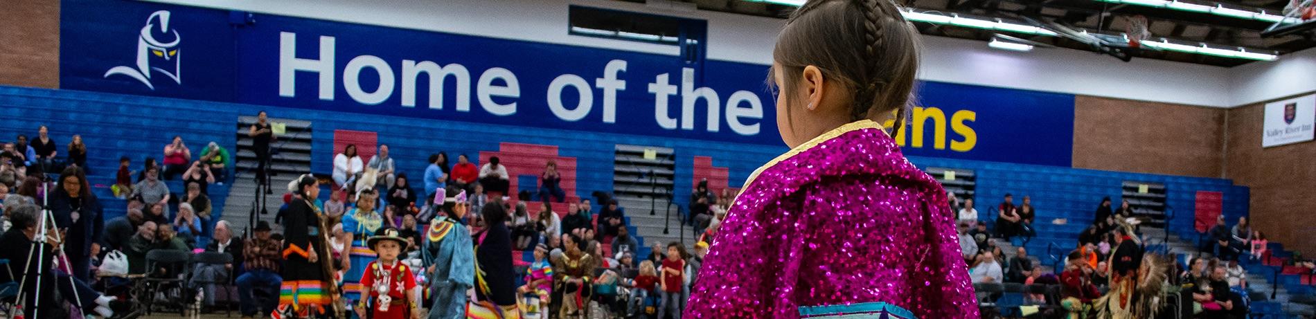 a native american child in regalia at a pow wow in the LCC gym