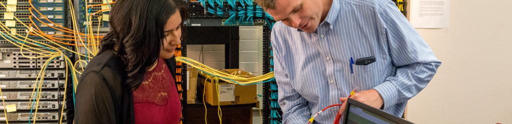 A computer science instructor teaches a student in a network server room