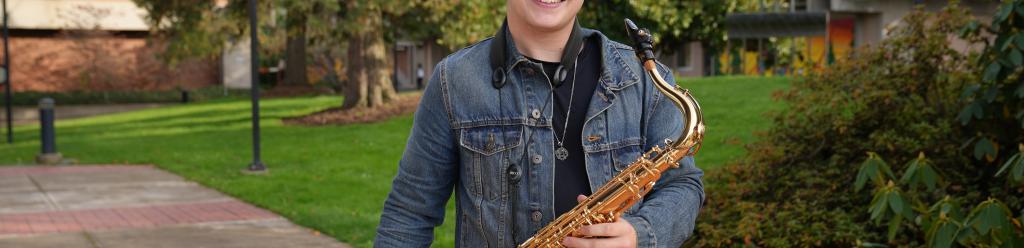 A music student in a jean jacket holding his saxophone and smiling