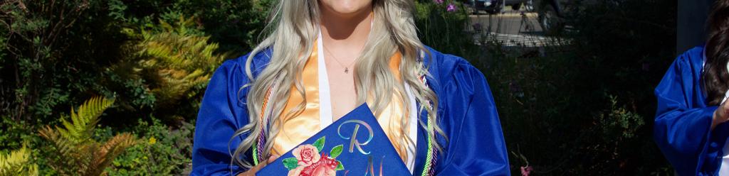 a nursing student, a young woman in blue gap and gown, shows off her decorated cap with a scientific and artistic heart