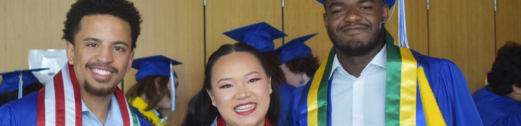 three graduating international students and friends, two Black men and an Asian woman, pose together and smile