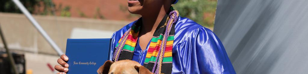 a graduating student, a young Black woman in blue cap and gown and a Black Student Union stole holds her dog and diploma