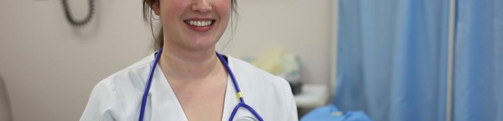 A BSN nursing student, a smiling young woman with a nose piercing, poses in a lab coat and stethoscope
