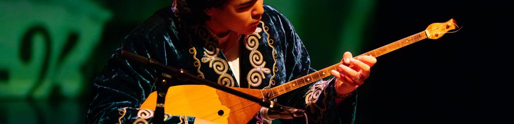 an international student, a young man, plays a traditional instrument on stage with dramatic lighting