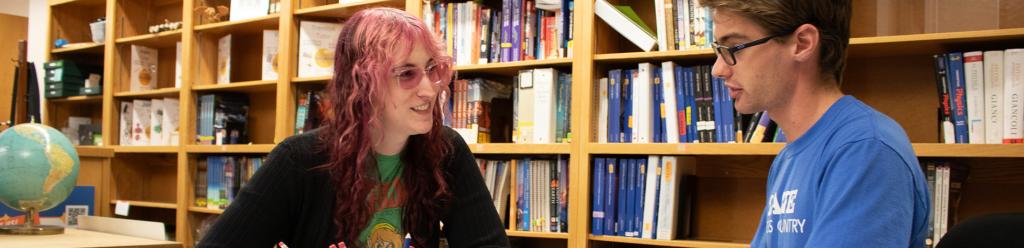 a transgender young woman and a young man in a cross country t shirt study together at the tutoring center