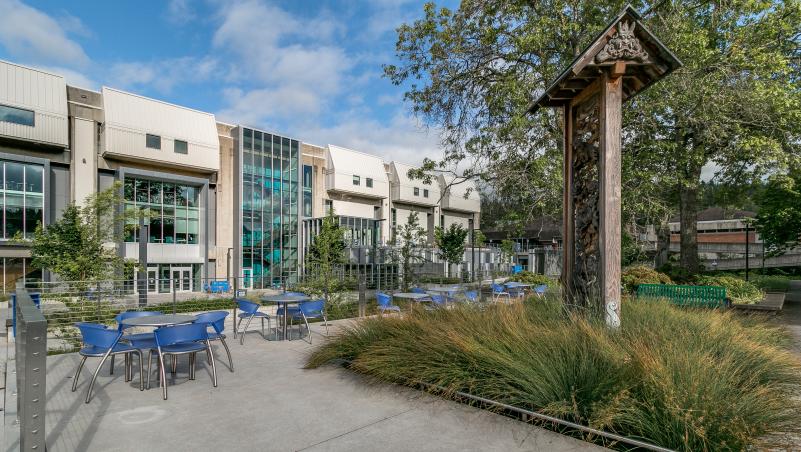 View of the center building with natural landscaping, chairs, tables, and a sculpture.