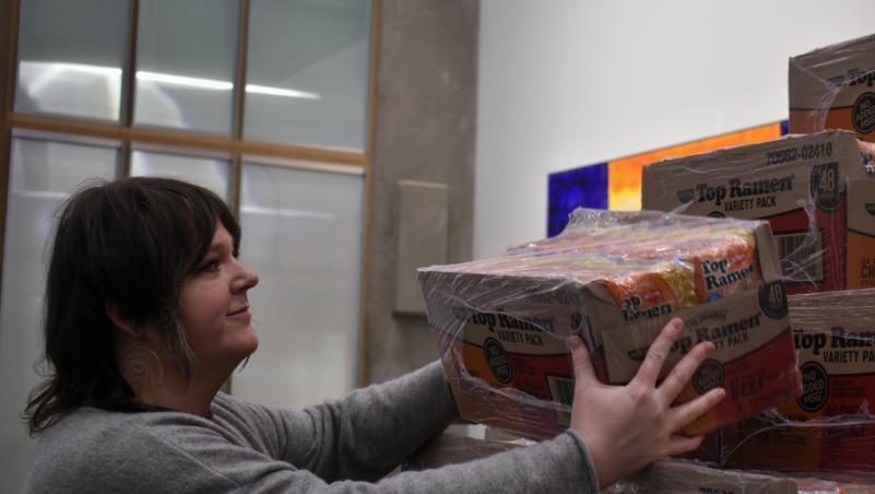 OER Librarian Meggie Wright places another case of ramen on the pyramid outside the library