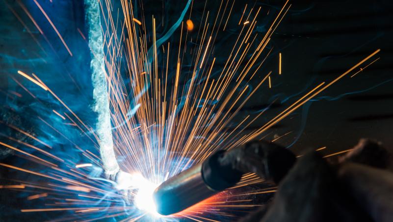 Sparks from welding metal and torch are seen on a black and blue background 