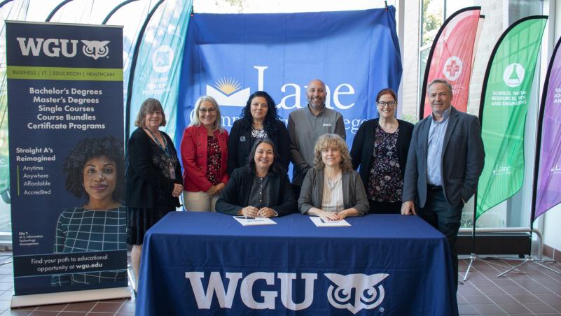 Representatives from Lane Community College and Western Governors University pose for a photo after signing a partnership agreement, with WGU and Lane banners displayed behind them.