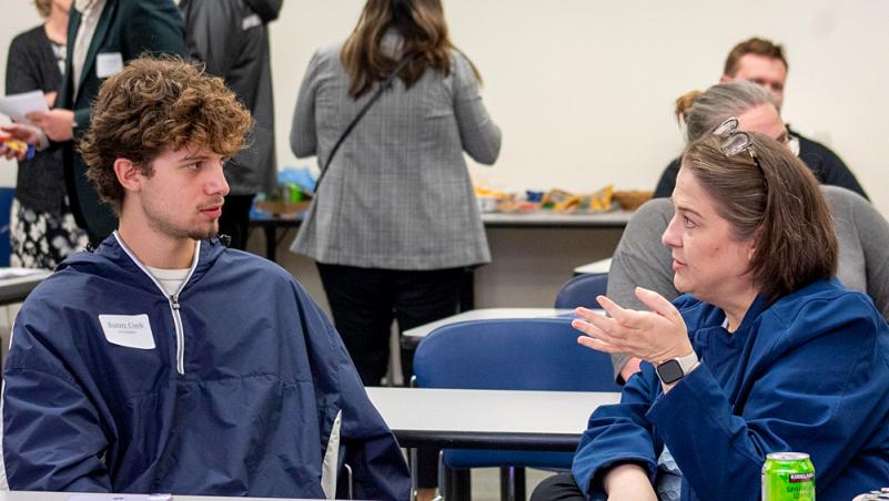 an LCC student, a young man with curly hair, listens intently to a community leader, an older woman, at the 2025 Mentor Connect Kickoff