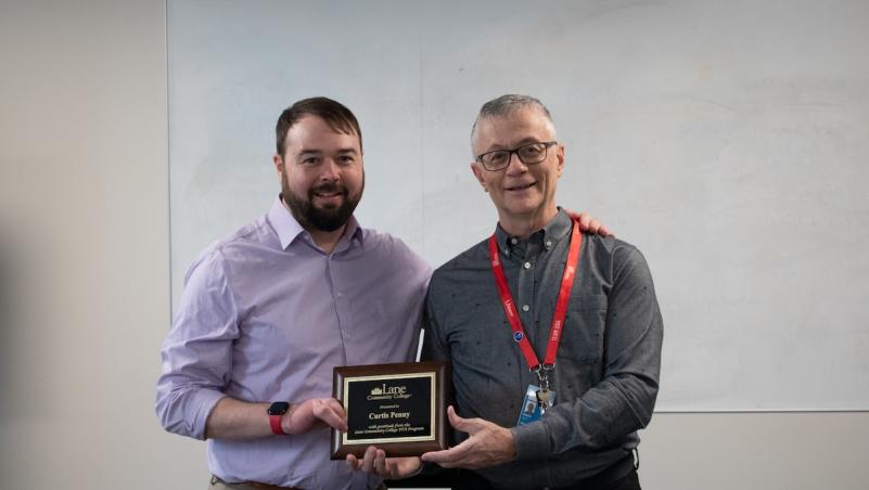 Physical Therapist Assistant instructor Marc Duyck gives an award to Prosthetist Curtis Penny, a smiling man with a hand difference
