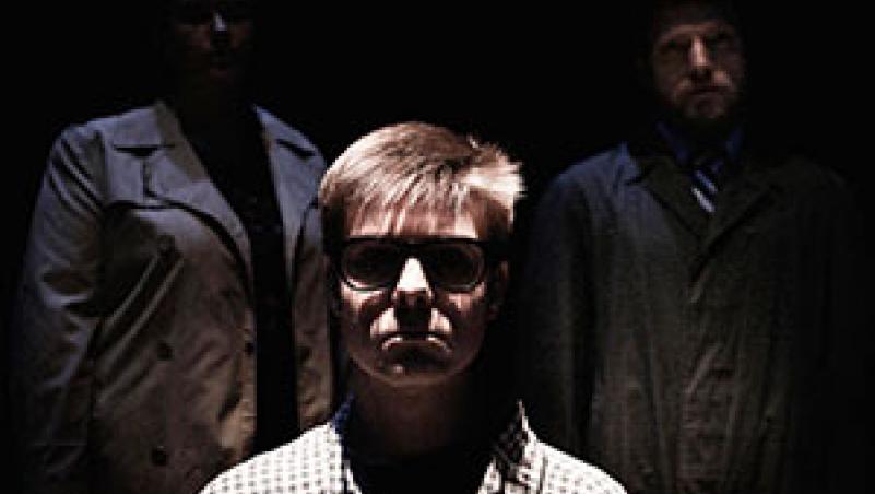 Some members of “The Birthday Party” image of young man in shadows, with two men behind him
