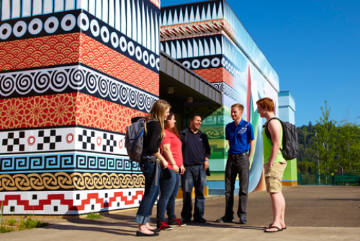 Five students standing together outside on a bright day