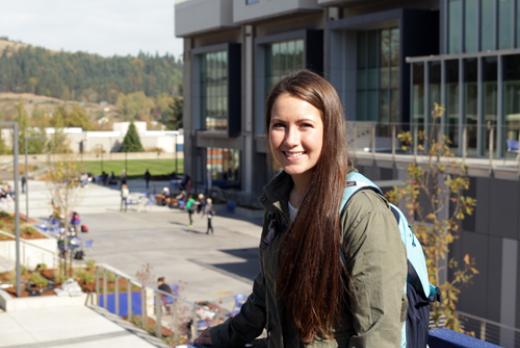 A young woman with a backpack smiling in front of Center Building on main campus