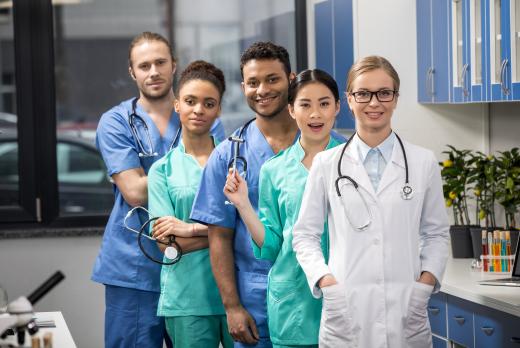 Group of diverse medical students or young healthcare professionals in scrubs and a lab coat, smiling in a clinical setting.