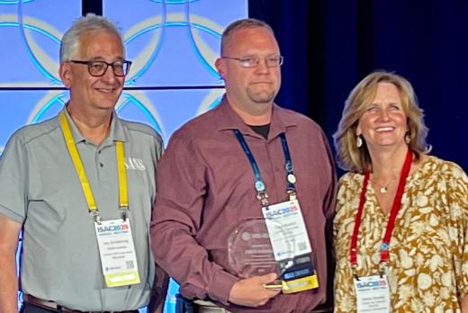 Fred Rankin receives an award at ISAC 2025 with two conference staff members.