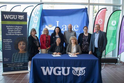 Representatives from Lane Community College and Western Governors University pose for a photo after signing a partnership agreement, with WGU and Lane banners displayed behind them.