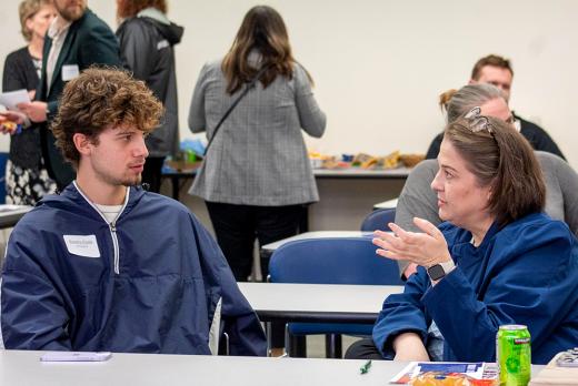an LCC student, a young man with curly hair, listens intently to a community leader, an older woman, at the 2025 Mentor Connect Kickoff