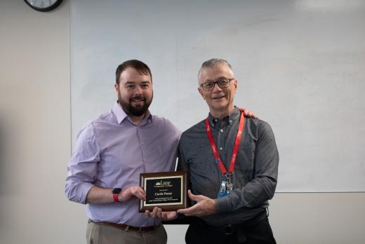 Physical Therapist Assistant instructor Marc Duyck gives an award to Prosthetist Curtis Penny, a smiling man with a hand difference