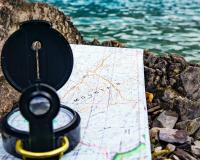 a compass sitting on a map on some rocks by a lake