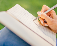 person writing on notepad propped up on their knees