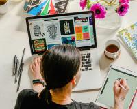 a graphic design program student gathering ideas for project using computer and sketch pad