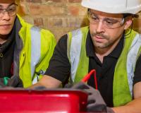 two electricians in gear working on a box