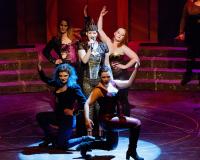 performers on stage pose while one speaks into a microphone