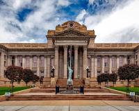 a courthouse in neoclassical style with a liberty statue in front and a dramatic blue sky behind